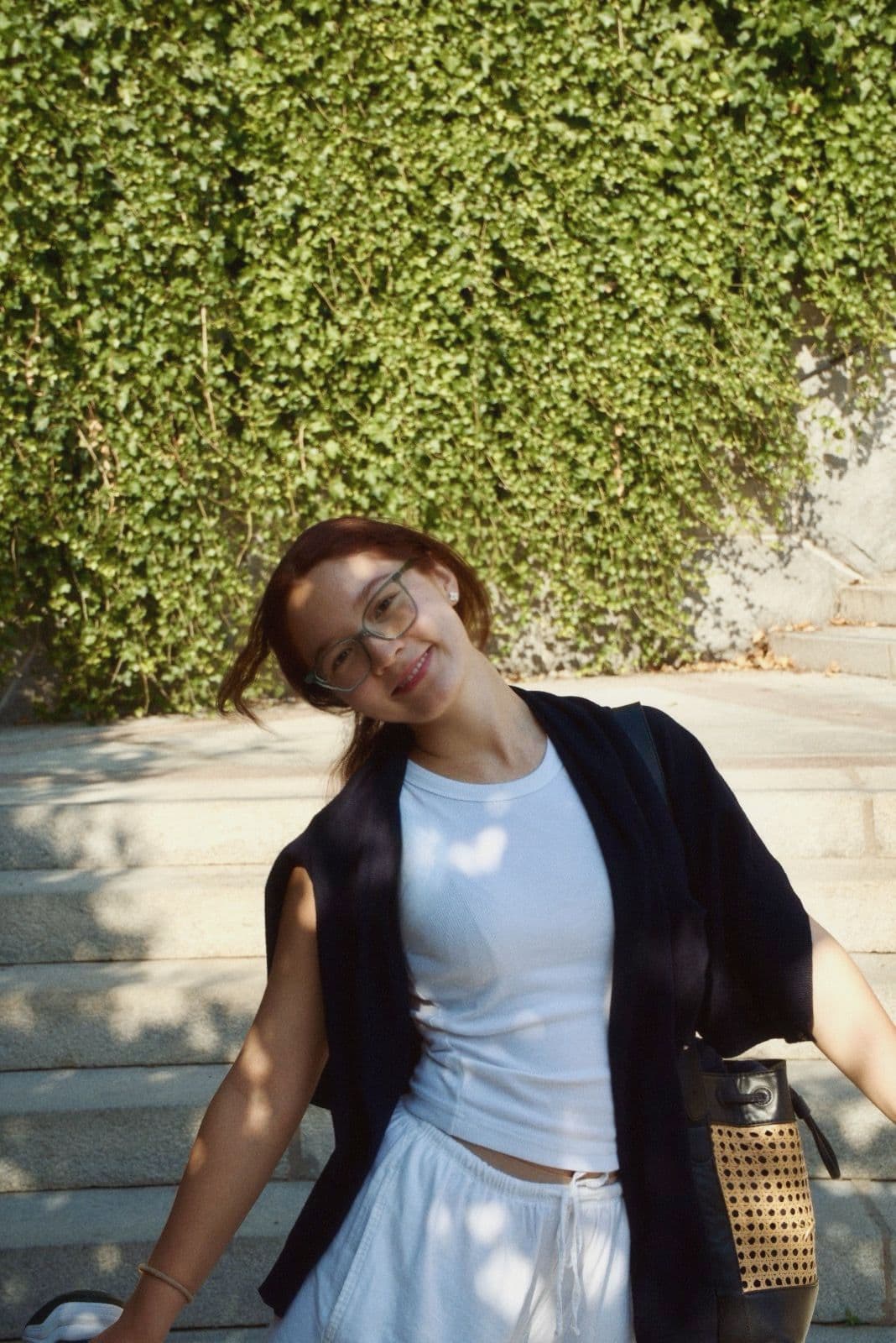 Kawsar smiling on stone steps in front of an ivy wall