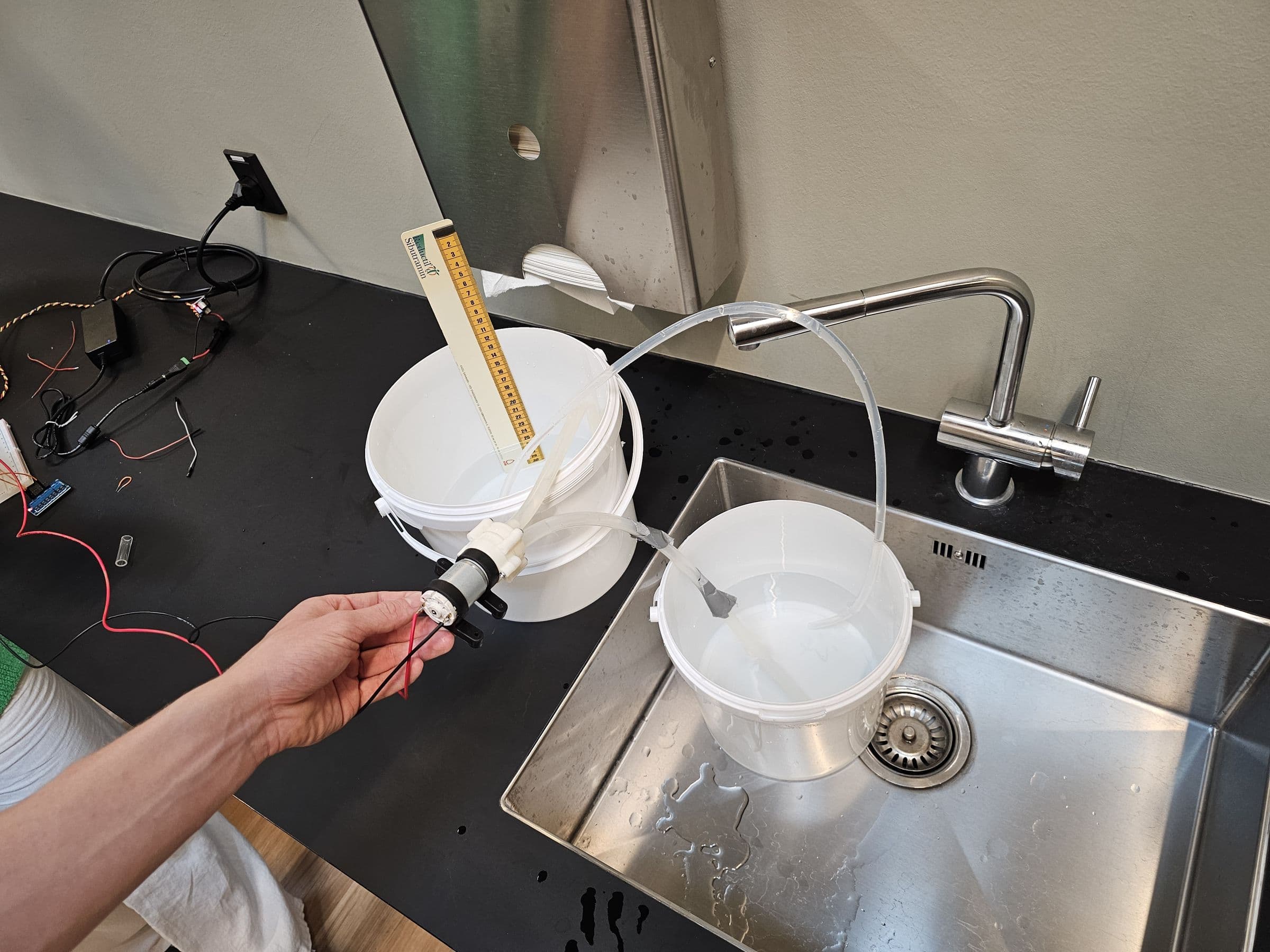 Two buckets joined by a siphon tube on a lab sink, with a ruler to read the water level