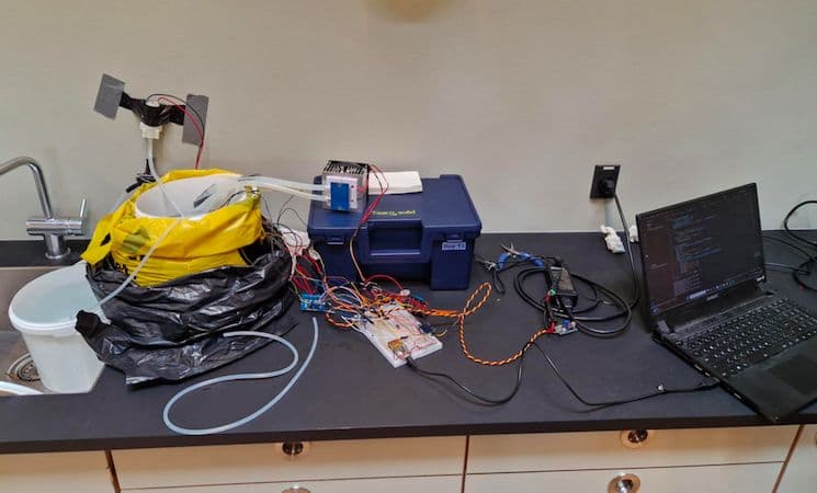The full bioreactor on a lab bench: the mussel bucket wrapped in yellow and black bags, a cooler box, breadboard electronics and a laptop