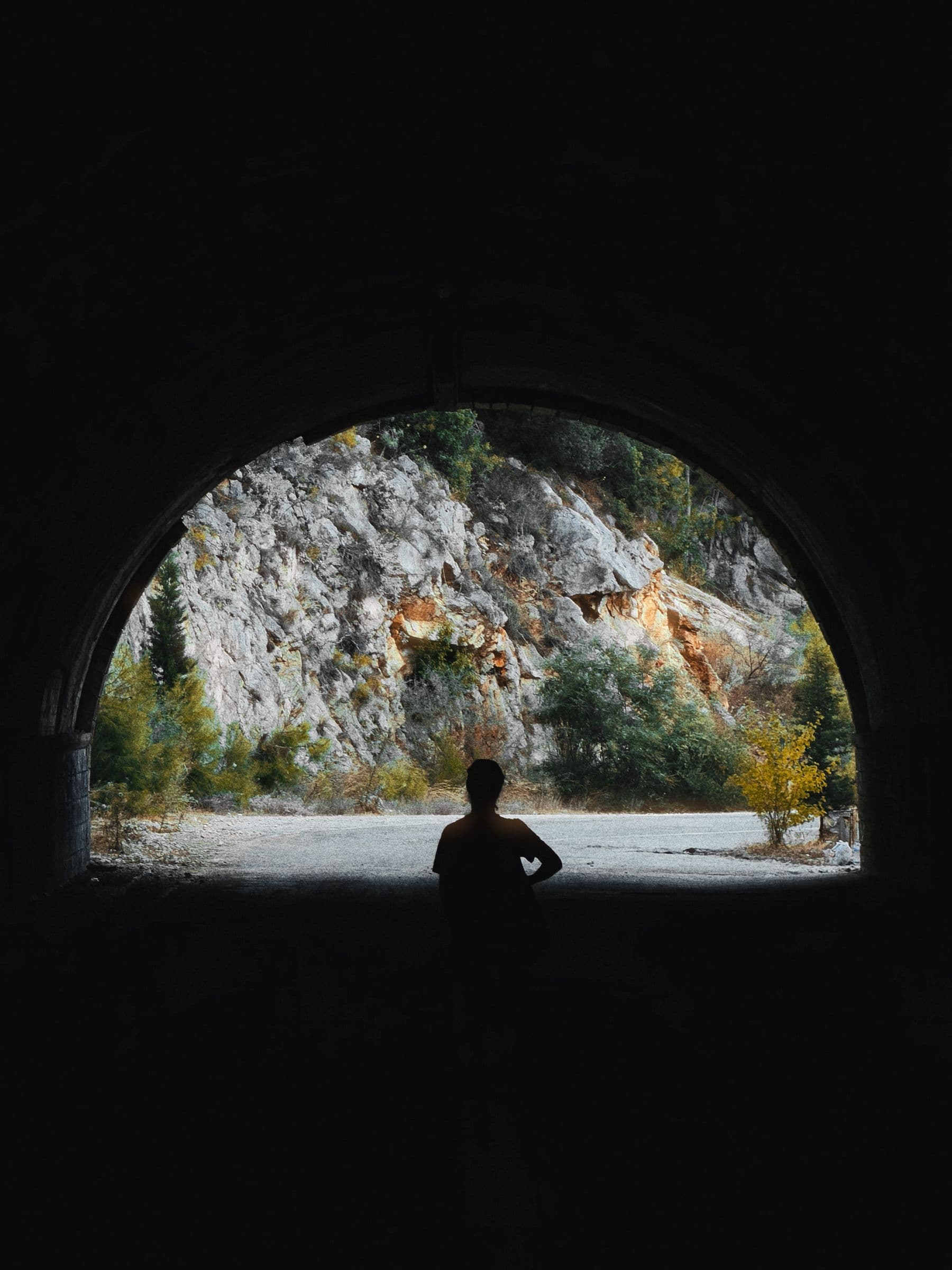 Kawsar silhouetted in a tunnel mouth, looking out at a rocky hillside